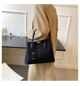Detail of black lychee grain leather tote bag with metallic tag on a camel trench coat