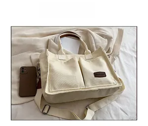 Detail of off-white canvas tote bag featuring double front pockets and brown leather logo patch