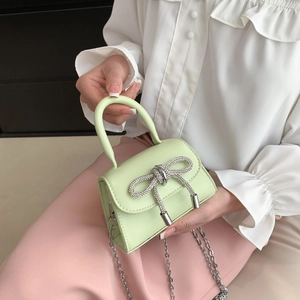 Light green mini handbag with rhinestone bow and silver chain strap held by model