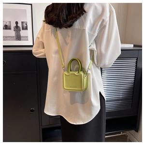 Détail du mini sac vert fluo avec poignée vert foncé contrastée sur chemise blanche