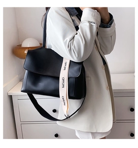 Détail d'un sac bandoulière en cuir noir avec sangle large à logo et bandoulière fine