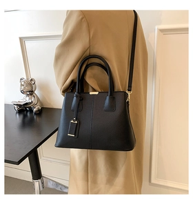 Modern black lychee leather tote bag with gold hardware shown as crossbody on model
