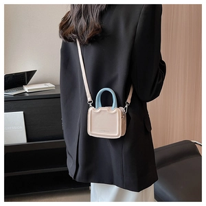 Sac bandoulière beige chic avec poignée bleue porté par un mannequin en décor urbain