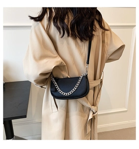 Close-up of a black crescent crossbody bag with silver chain worn over a beige trench coat