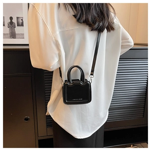Détail du mini sac carré en cuir noir avec double poignée et lettrage de mode chic