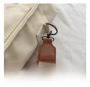 Detail showing premium gun-metal D-ring and brown leather strap on off-white canvas tote bag