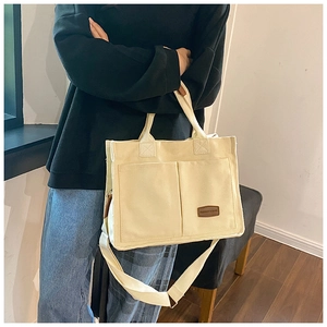 Detail view of cream canvas tote bag showing double front pockets and leather label