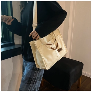 Detail of canvas tote bag showing front pocket and dark brown leather logo patch