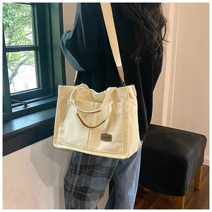Close-up of off-white canvas tote with dual front pockets and brown leather brand label