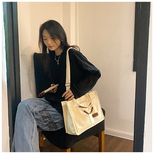 Detail of off-white canvas tote bag featuring brown leather handles and a large outer pocket