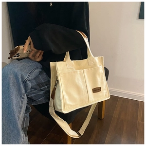 Detail of cream canvas tote bag featuring front twin pockets and leather patch accents