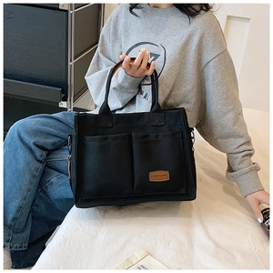 Detail of black canvas tote bag with dual front pockets and brown leather brand label