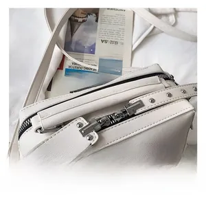 Close-up of white crossbody bag with silver double zippers and rivet detail on lychee leather