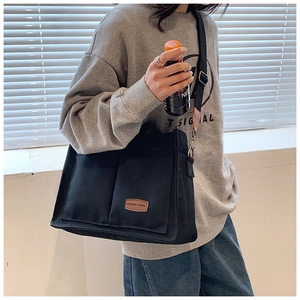 Detail view of black canvas tote bag showing the leather logo patch and wide strap