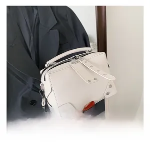 Close-up of white crossbody bag with silver rivet studs and metallic corner guards