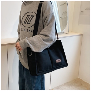 Detail of black canvas tote bag showing front pockets and leather brand patch