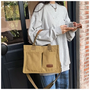 Detail shot of khaki canvas tote bag with front square pockets and leather logo tag