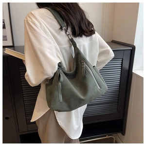 Detail of dark green suede hobo bag with dual silver zippers shown on shoulder
