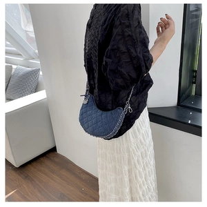 Detail of denim quilted crescent bag with silver chain strap worn by a model