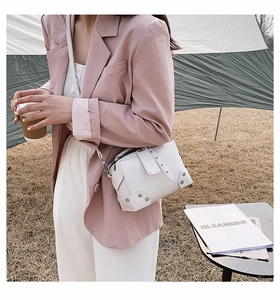 Close-up of white leather crossbody bag featuring silver rivet trim and metal buckle