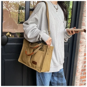 Detail of khaki canvas tote bag with large front pockets and brown leather trim accents