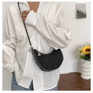Detail of black quilted denim crescent bag with silver metal chain strap and zip