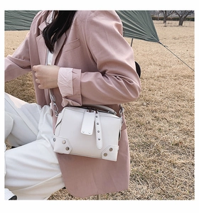 Detailed view of a white crossbody square bag with silver studs on outdoor lawn