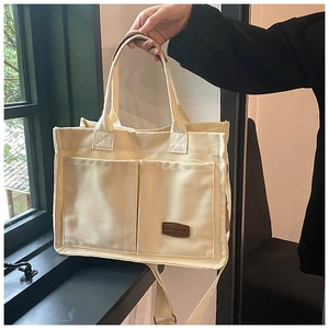 Detail of minimalist canvas tote with dual front pockets and brown leather tag