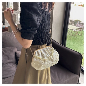 Détails d'un sac à main beige plissé avec ornements en perles et fine bandoulière dorée