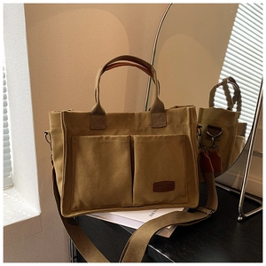 Detailed close-up of a khaki canvas tote bag featuring functional front pockets and leather labels