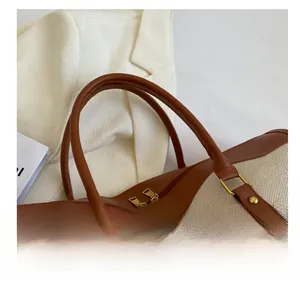 Close-up of beige canvas tote with brown leather handles and gold metal hardware details