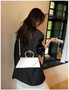 Detail showing the silver irregular metal handle and asymmetric design of the white leather bag