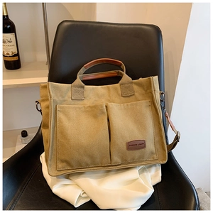 Detail of khaki canvas tote bag with front pockets and leather trim on a silk cloth