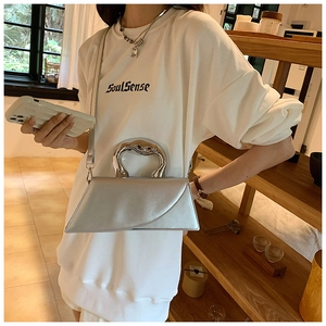 Detail of silver trapezoid handbag with sculptural metallic handle in a warm setting