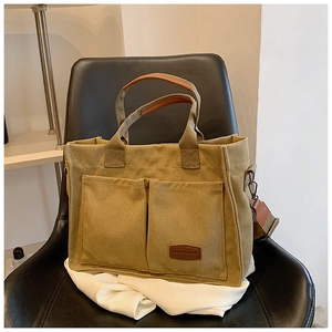 Detail view of khaki canvas tote bag with leather handles and dual front patch pockets