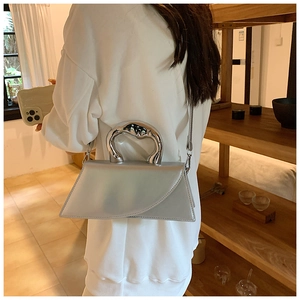 Detail of silver trapezoid handbag featuring a liquid metal style irregular top handle