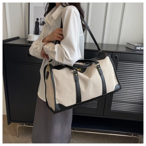 Detail view of large beige canvas travel tote with black leather trim and adjustable strap
