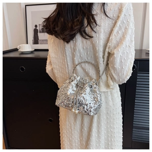 Detail view of a silver sequin bucket bag with pearl drawstring and metal chain strap