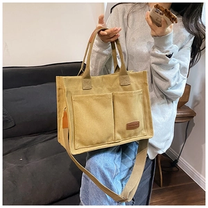 Close-up of ginger yellow canvas tote bag featuring front pockets and brown leather logo tag