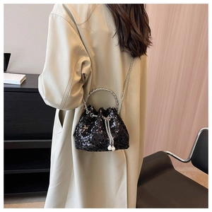 Detail of black sequin bucket bag with pearl drawstring and silver chain strap on model