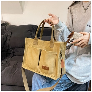 Detail of a mustard canvas tote bag featuring double front pockets and brown leather label