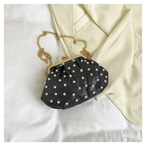 Détail du sac à fermoir noir perlé avec chaîne dorée sur fond de tissu blanc doux