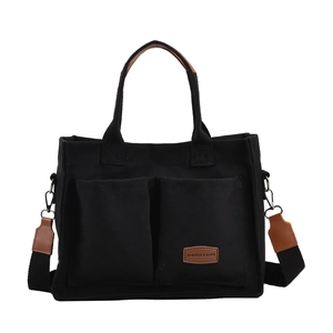 Close-up of black canvas tote bag with brown leather patches and two front pockets