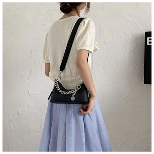 Sac bandoulière demi-lune noir avec chaîne argentée porté par un mannequin sur fond uni
