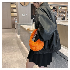 Detail of bright orange quilted dumpling bag featuring textured square pattern and soft folds