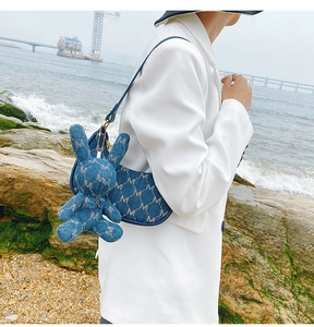 Détail du sac croissant en denim bleu avec motif M blanc et pendentif lapin
