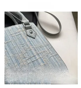 Detail shot of the light blue woven texture with silver metal handle hardware on the handbag