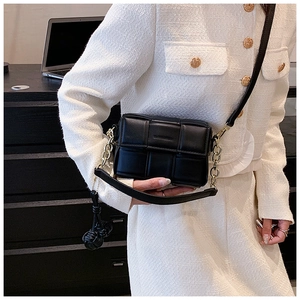 Détail d'un sac bandoulière tissé noir avec chaîne dorée et pompon sur une veste blanche