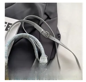 Detail of light blue tweed handbag featuring a woven handle and adjustable leather strap