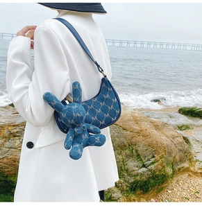 Détail du sac croissant en denim bleu avec motif M et breloque lapin en bord de mer